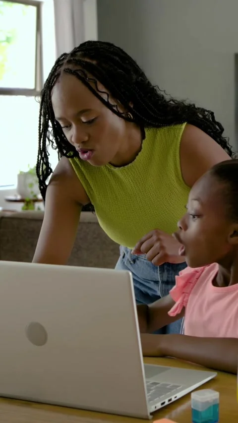 Vertical video: Leaning mother in lime top guiding daughter using laptop at Stock Footage 348491153
