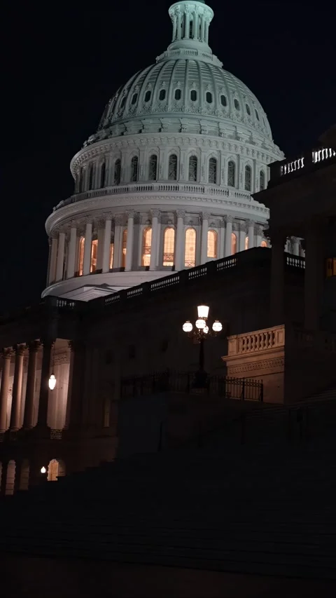 Vertical video to left showing the US Capitol with lights and flags waving in Stock-Footage 314658382