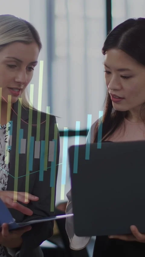 Vertical video: Left woman tapping blue tablet sparking charts over PC as women Stock Footage 333527755