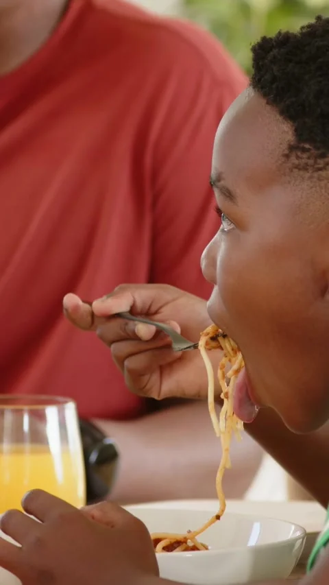 Vertical video: Lifting fork, boy in green shirt twirling spaghetti at table Stock Footage 348490255