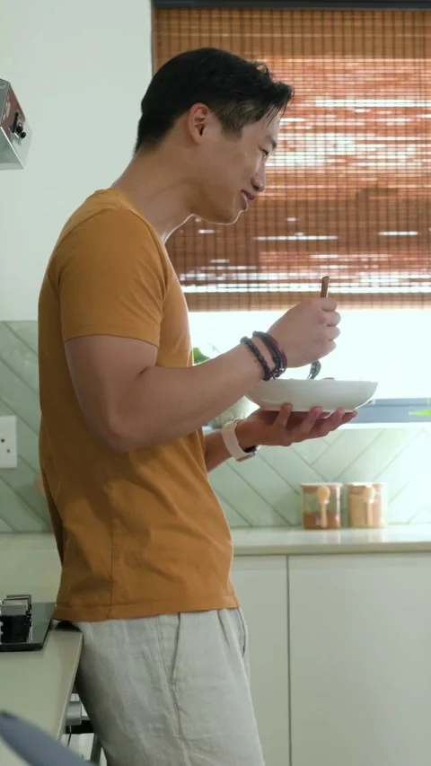 Vertical video: Lifting fork, man in mustard tee tasting to check flavor at Stock Footage 348273422