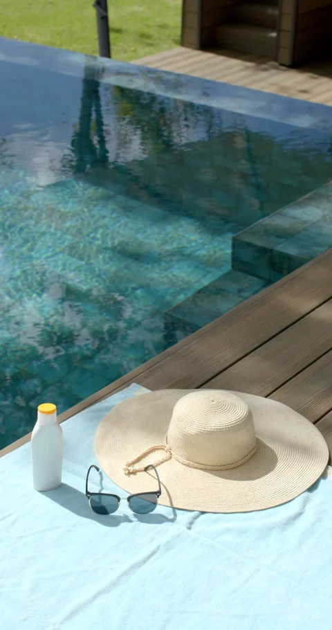 Vertical video: Light breeze rippling pool as hat, sunglasses, sunscreen are Stock Footage 345040782
