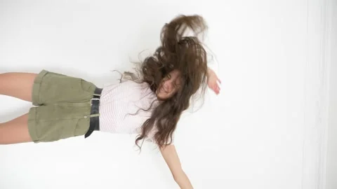Vertical video. long-haired slender teenage girl cheerfully dancing on a white Stock Footage 147667369