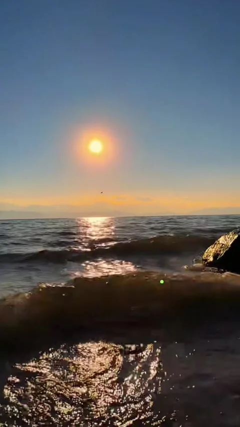 Vertical video low angle shot of waves crashing on shore at golden sunset wi Stock Footage 327631617