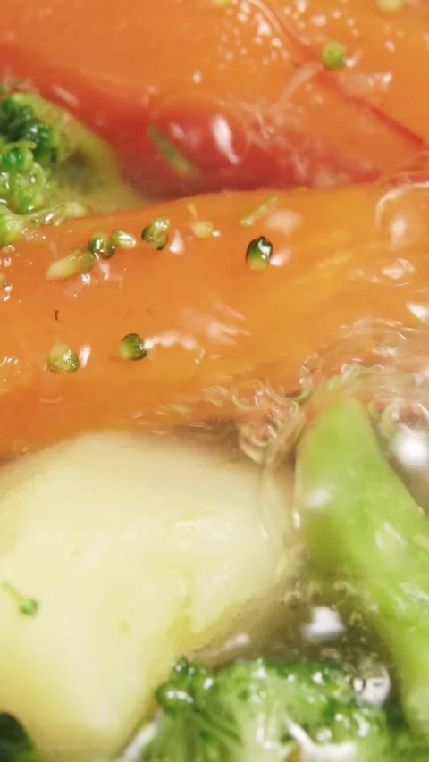 Vertical video macro view of fresh carrots and broccoli boiling in bubbling Stock Footage 348026597