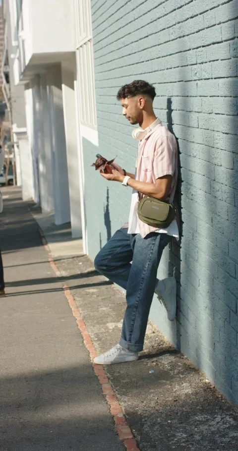 Vertical video: Man in 20s checking phone then opening pastry, eating on Stock Footage 346599904