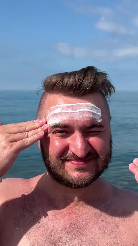 Vertical video. Man applies sunscreen cream to face on sea beach Stock Footage 313363449