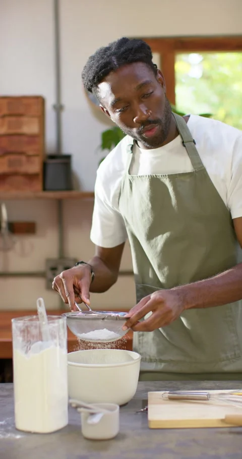 Vertical video: Man in apron in kitchen scooping flour from jar sifting sieve Video stock 345493482