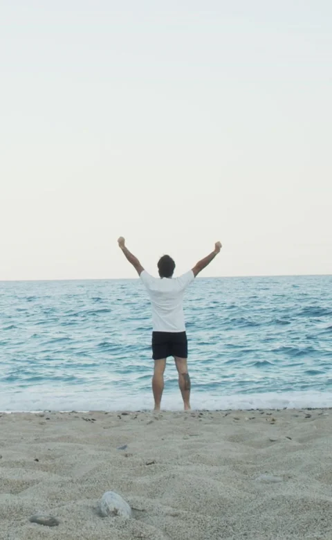 Vertical video. Man with arms raised on a beach during a sunset Stock Footage 207860596
