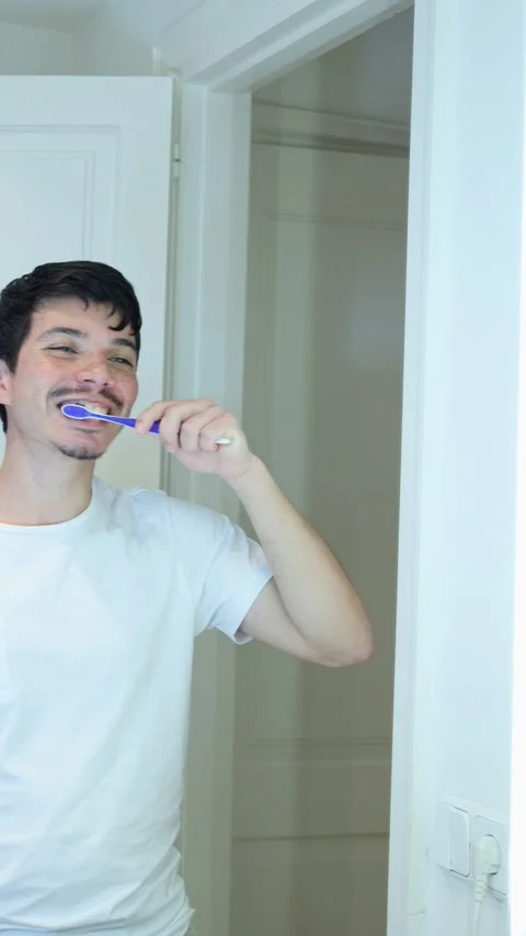 Vertical video of a man brushing his teeth in the bathroom of his house in .. Stock Footage 297474441