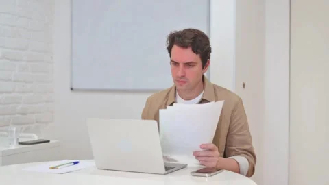 Vertical Video, Man Celebrating Paperwork Documents while Working on Laptop Stock Footage 312914381
