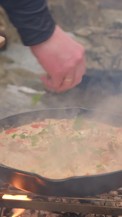 Vertical video of man cook baked chicken with sun-dried tomatoes on bonfire Stock Footage 299703283