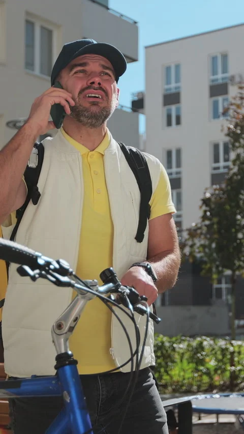 Vertical video. Man courier with yellow backpack with bicycle in city Видео 344375694
