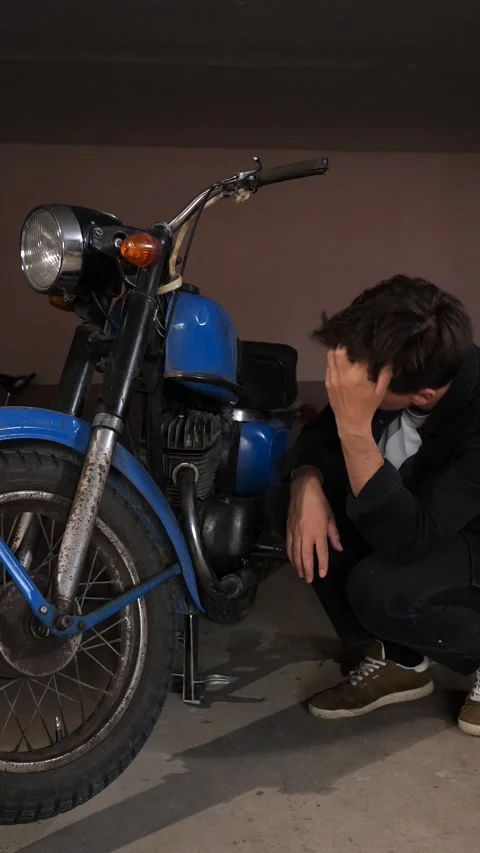 Vertical video man crouching in a garage, intently thinking and looking at an Stock Footage 342765668
