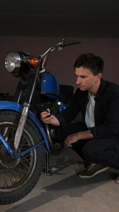 Vertical video man crouching inspecting the engine of a vintage blue motorcycle Stock Footage 342769917