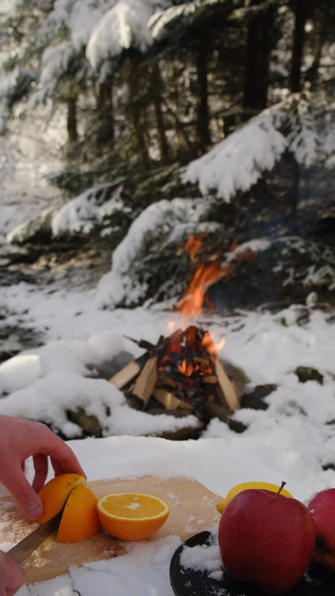 Vertical video of man cuts fresh orange on wooden board on background bonfire Stock Footage 300945004