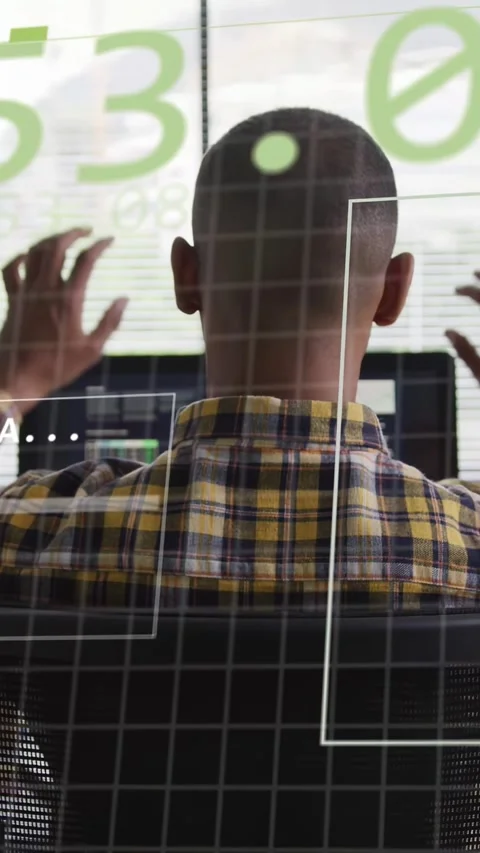 Vertical video: Man at desk stretching as green HUD overlaying monitors after Stock Footage 333840211
