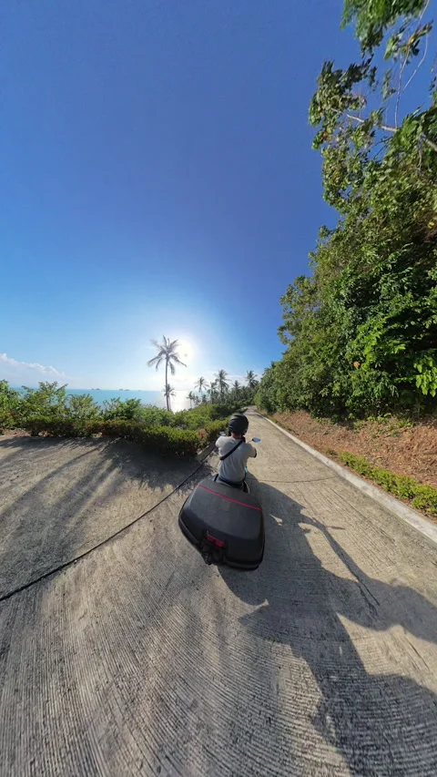 Vertical video. Man Driving Scooter on Palm Tree Road With Ocean View in Rear Stock Footage 314039074