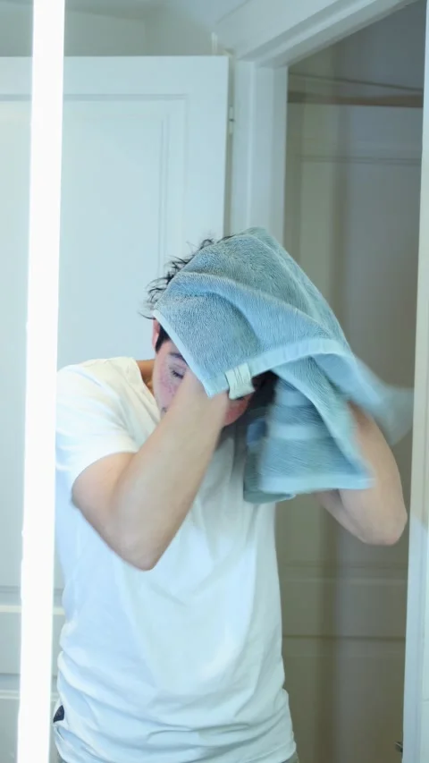 Vertical video of man drying his hair with a towel in front of a bright mirro Stock Footage 297666151