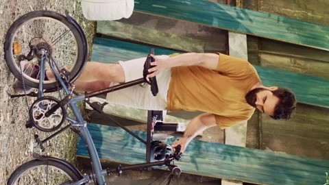 Vertical video Man ensuring bicycle function in yard 스톡 동영상 248471226