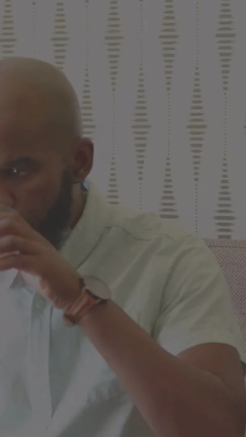 Vertical video: Man entering, sitting on sofa, drinking, using phone; tech UI Stock Footage 333953270
