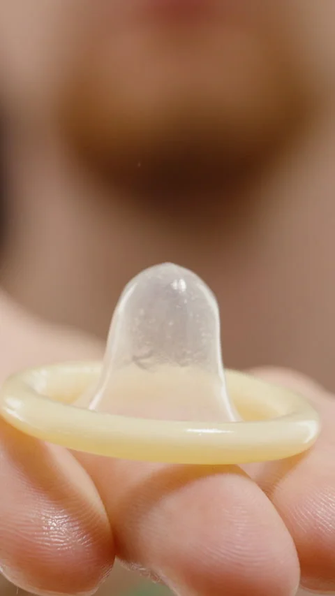 Vertical video. A Man Holding a Condom in an Outstretched Hand Against a Black Stock Footage 301044174