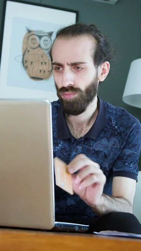 Vertical video. A man at home, upset while holding a credit card and lookin.. Stock Footage 296889634