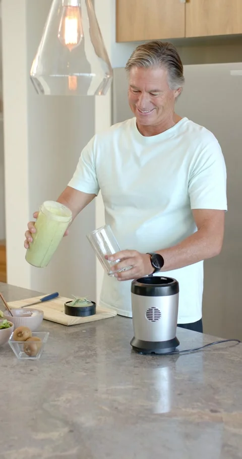 Vertical video: Man inspecting blender cup at kitchen island, pouring shake into Video stock 345218466