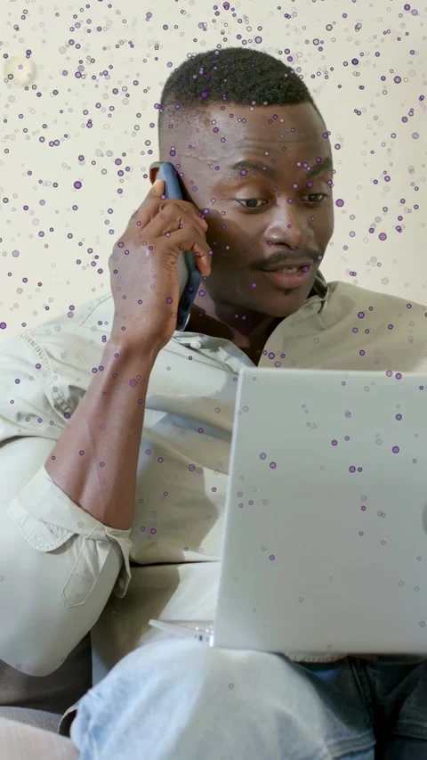 Vertical video: Man looking up from laptop speaking, holding phone, dot overlay Stock Footage 333777163