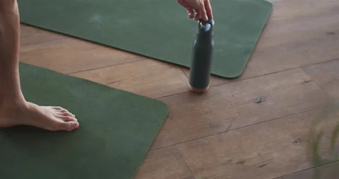 Vertical video: Man lowering dark bottle onto floor beside green mat, placing Stock Footage 336844882