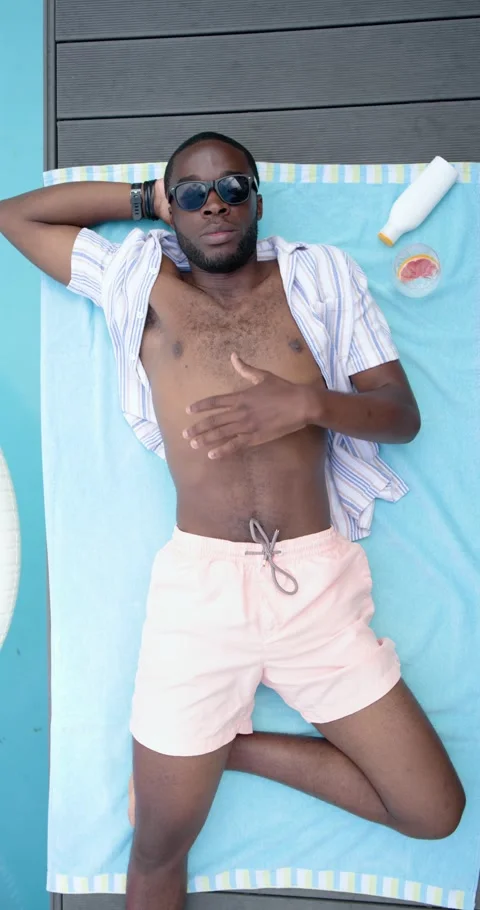 Vertical video: Man lying at pool in shirt, sun causing shifting, smiling by Stock Footage 345218496