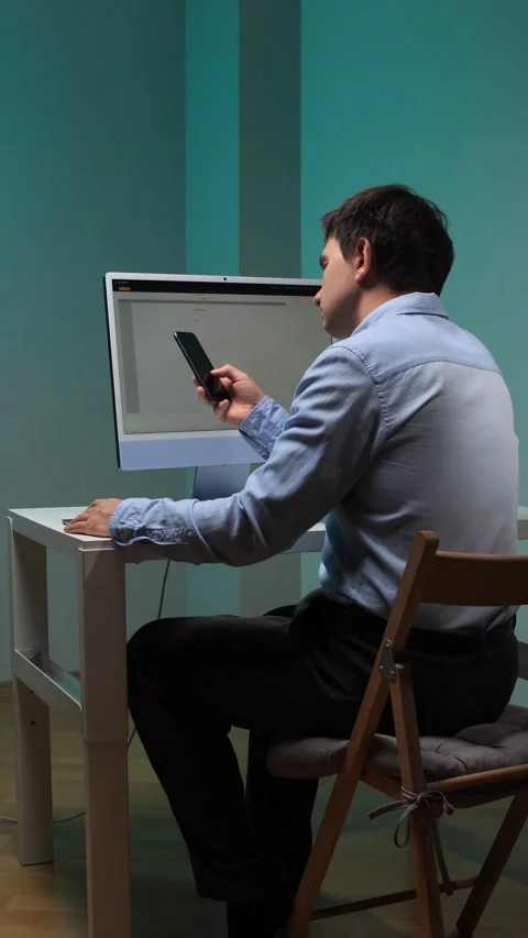 Vertical video man multitasking on a smartphone and computer, working from his Stock Footage 345529991