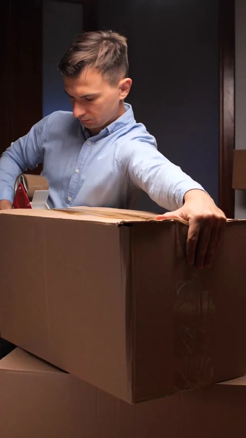 Vertical video Man packing cardboard box with tape dispenser Stock Footage 318981665