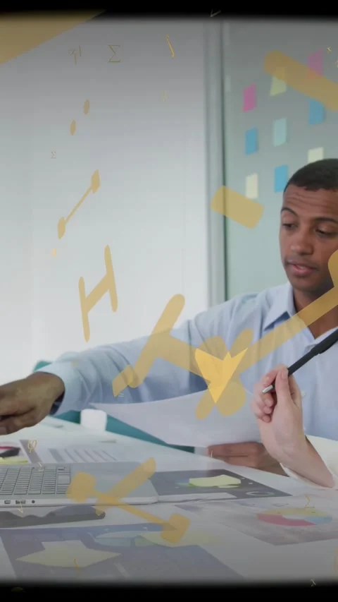 Vertical video: Man pointing at laptop, causing yellow overlay across table 動画素材 333596025