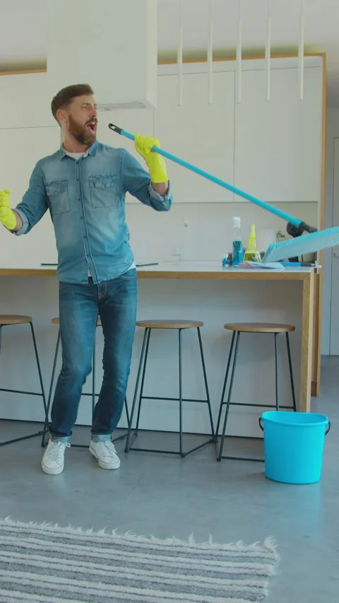 Vertical Video Man in protective gloves is singing using a mop and dancing Stock Footage 337994601
