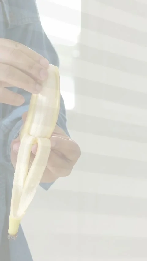 Vertical video: Man pulling back banana peel with right hand, rotating fruit, Stock Footage 337540618