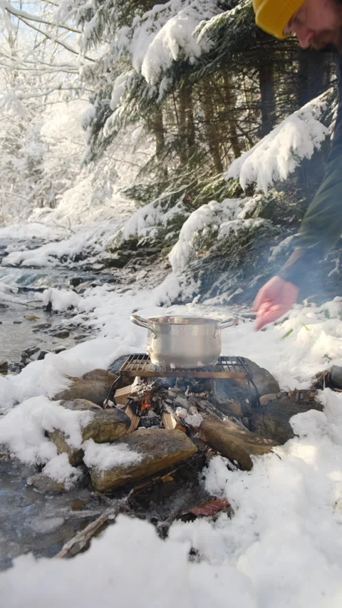 Vertical video of man put pot on bonfire, cooking mulled wine near river Stock Footage 300940008