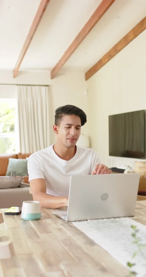 Vertical video: Man reading puzzling laptop message at dining table, checking Stock Footage 345396498