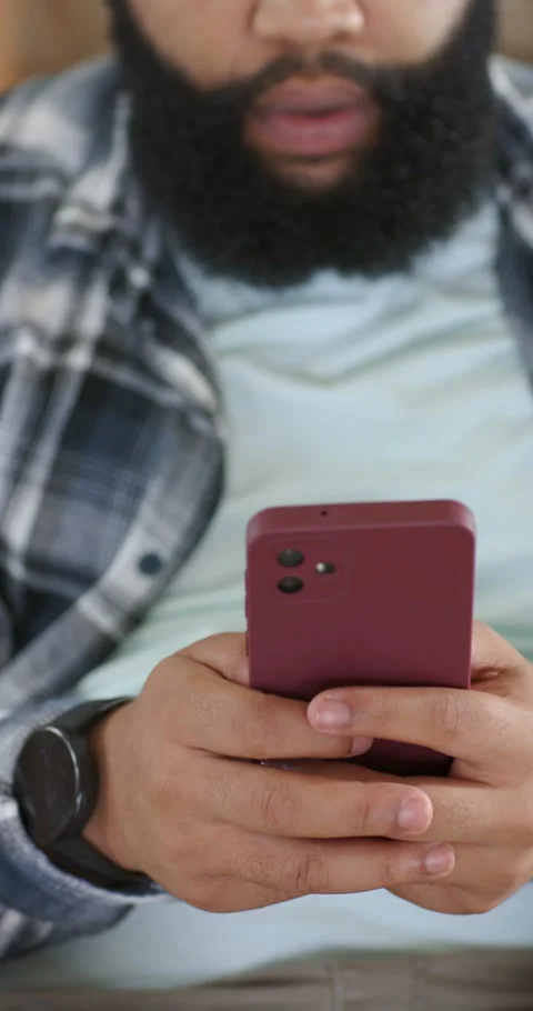 Vertical video: Man reading text to reply, tapping maroon phone on couch, Stock Footage 345219363
