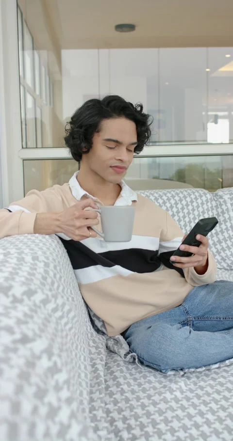 Vertical video: Man scrolling smartphone and sipping grey mug while leaning on Stock Footage 345217690