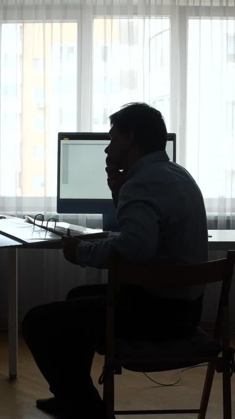 Vertical video man silhouette at a computer desk in a bright office window Stock Footage 345530475