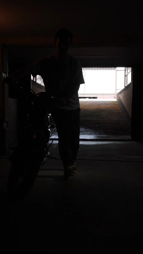 Vertical video man in silhouette pushing a classic motorcycle, exiting a dark Stock Footage 342768470