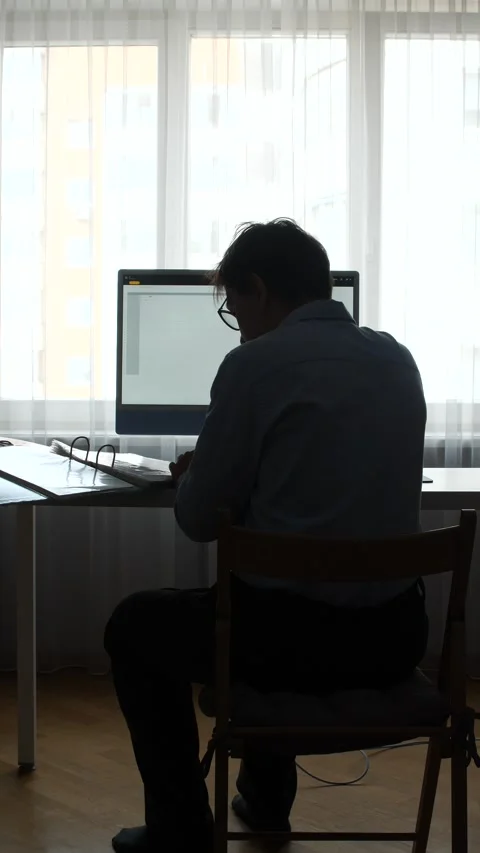 Vertical video man in silhouette sitting at desk, working on computer with Stock Footage 345532069