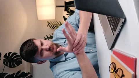 Vertical video of man sit at table with laptop and experiencing pain in fingers Stock Footage 234982585