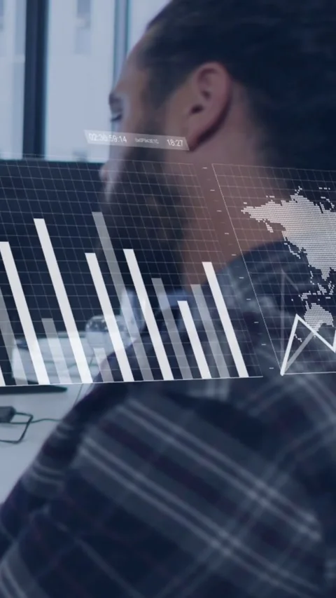 Vertical video: Man sitting at desk monitor loading, graphs morphing over him Stock Footage 334541203