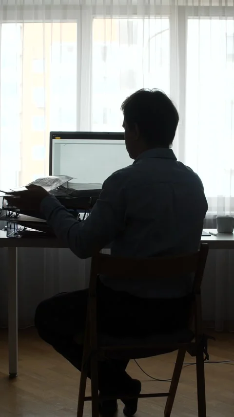 Vertical video man sitting at a desk and working on a computer while reviewing Stock Footage 345531587