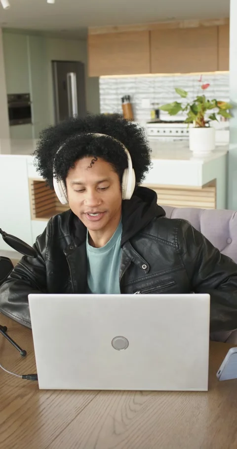 Vertical video: Man sitting in kitchen wearing headphones, speaking into mic, Stock Footage 346723872