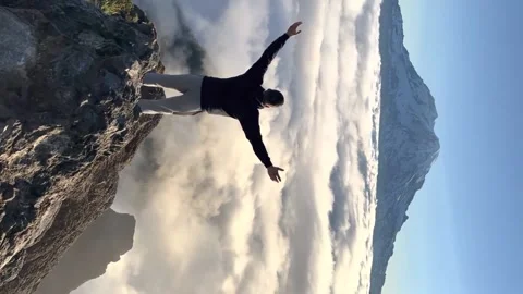 Vertical video. a man stands on a mountain above the clouds with outstretched Stock Footage 218308847