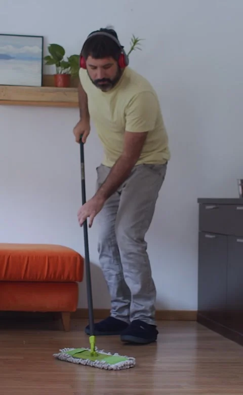 Vertical video. Man sweeping the floor of an apartment while listening to music Stock Footage 247761767