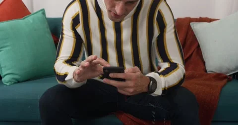 Vertical video: Man tapping phone on couch scrolling for app content and 库存影片 330540328